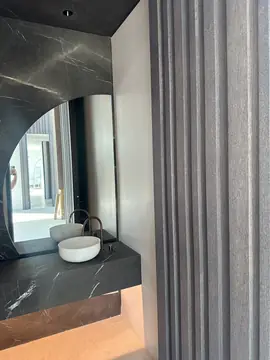 Lavabo junto a panel de listones. Encimera negra de veta blanca con lavabo de apoyo, vista junto a un revestimiento de listones verticales.