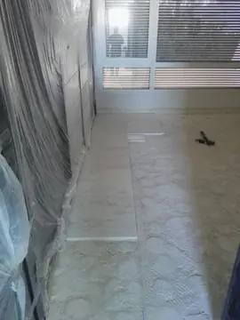 Arranque del pavimento junto a la ventana. Primeras piezas blancas colocadas a lo largo de la pared protegida con plástico, con el adhesivo extendido en el resto de la estancia.