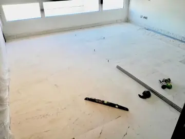 Pavimento blanco veteado recién colocado. Estancia con el suelo de piezas grandes blancas con veta gris ya asentado, con nivel y regla aún sobre el pavimento.