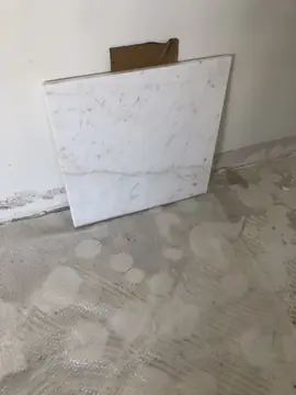 Pieza blanca veteada apoyada en la pared. Pieza blanca con vetas grises finas apoyada contra la pared de una estancia en obra, con el suelo protegido delante.
