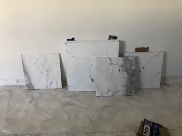 Piezas de distinto veteado junto a la pared. Piezas blancas con veteado gris y violáceo de distinta intensidad, apoyadas en la pared de una estancia en obra.
