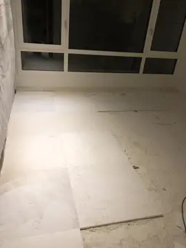 Colocación del pavimento junto al ventanal. Piezas blancas grandes colocadas junto a la pared protegida, con parte del suelo aún con el adhesivo a la vista.