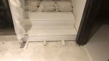 Arranque de peldaños en piezas blancas. Peldaños blancos recién colocados sobre cuñas, con el ladrillo aún a la vista por encima y un poste envuelto en plástico.