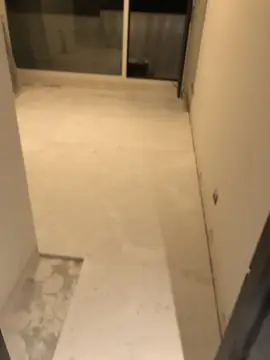Pavimento colocado en un pasillo. Pasillo con el pavimento de piezas blancas asentado y una esquina todavía con el adhesivo a la vista.