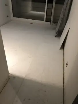 Estancia con el pavimento blanco colocado. Suelo de piezas blancas grandes ya colocado hasta la cristalera, con algunas piezas sueltas apoyadas en la pared.