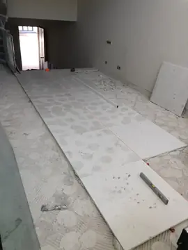 Colocación del pavimento a cordel. Hileras de piezas blancas recién colocadas siguiendo un cordel, con nivel y regla sobre el suelo y el adhesivo a los lados.