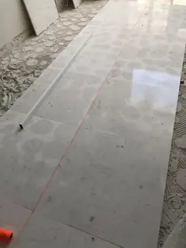 Hileras de pavimento alineadas a cordel. Piezas blancas colocadas en hilera siguiendo un cordel naranja, con una regla de aluminio sobre el suelo y el adhesivo a los lados.