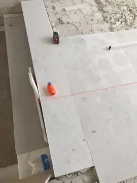 Replanteo del pavimento con láser y cordel. Nivel láser y cordel sobre las primeras piezas blancas colocadas, marcando las líneas para seguir con el pavimento.