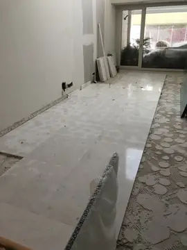 Estancia con el pavimento a medio colocar. Franja de piezas blancas de acabado brillante colocada hacia la cristalera, con el resto del suelo aún con adhesivo.