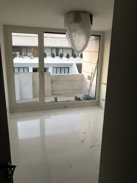 Estancia con pavimento blanco pulido. Pavimento de piezas blancas pulidas con veta gris y rodapié a juego, visto desde la puerta hacia la terraza.