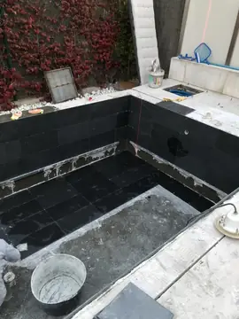 Piscina con el vaso en revestimiento. Muros y parte del fondo de la piscina revestidos con piezas negras, con la línea del láser marcando la colocación.