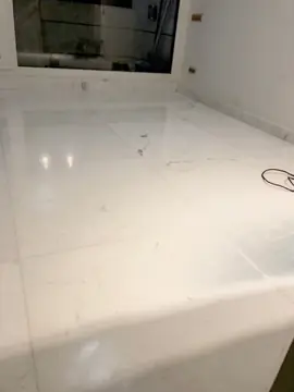 Pavimento blanco pulido junto a la ventana. Suelo de piezas blancas pulidas con veta gris suave y rodapié a juego, con reflejos de luz junto a la ventana.