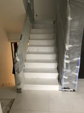 Escalera con peldaños blancos. Tramo de escalera con huellas y tabicas en piezas blancas de veta suave, con la barandilla aún protegida con plástico.