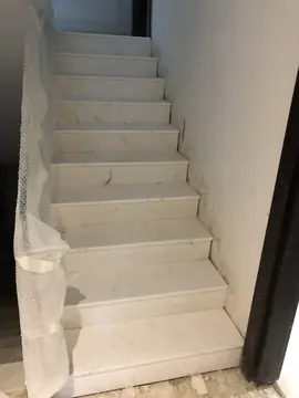Escalera revestida en piezas blancas veteadas. Peldaños con huella y tabica blancas de vetas grises, con la barandilla aún envuelta en plástico burbuja.