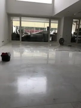 Salón con el suelo blanco en obra. Salón a doble altura con suelo blanco brillante en piezas grandes, con un ventilador y cables aún sobre el pavimento.