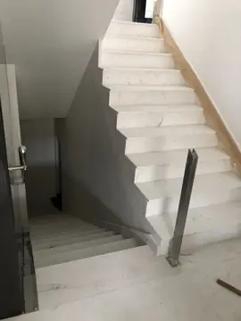 Escalera de peldaños blancos en obra. Escalera con un tramo de subida y otro de bajada en peldaños blancos veteados, un poste de barandilla y la pared protegida con papel.
