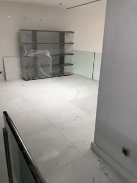 Distribuidor con pavimento blanco. Suelo blanco veteado en gran formato junto a la barandilla de vidrio, con una estantería aún embalada al fondo.