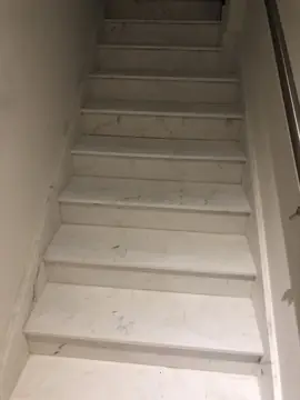 Escalera recta de peldaños blancos. Tramo recto con huellas y tabicas blancas de veta gris, zanquín a juego y pasamanos metálico.