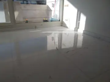 Pavimento pulido con entrada de sol. Suelo blanco pulido con veta gris en piezas grandes, iluminado por el sol que entra por la ventana.