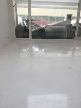 Pavimento pulido frente a la terraza. Suelo blanco pulido del salón con reflejo de los ventanales y los muebles de exterior aún embalados.