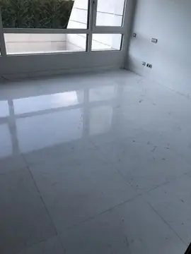 Pavimento pulido en estancia vacía. Suelo blanco de veta gris en gran formato con el reflejo de la ventana y rodapié a juego.