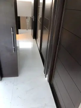 Pasillo con suelo blanco y puertas oscuras. Pavimento blanco pulido en gran formato entre puertas y paneles oscuros.