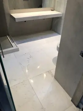 Baño con encimera volada y suelo blanco. Baño con encimera volada en tono claro, paredes grises y pavimento blanco veteado junto al plato de ducha.