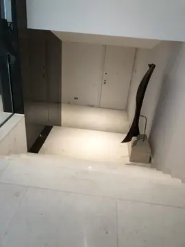 Escalera de bajada al vestíbulo. Peldaños y rellano en piezas blancas que bajan a un vestíbulo con escultura y puertas claras.