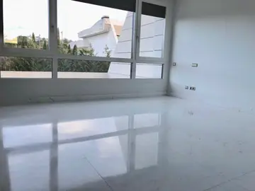 Estancia con ventanal corrido. Pavimento blanco pulido en piezas grandes que refleja el ventanal corrido y la luz exterior.