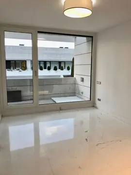 Estancia con lámpara y salida a terraza. Suelo blanco con veta gris en gran formato y rodapié a juego, con el reflejo del ventanal hacia la terraza.