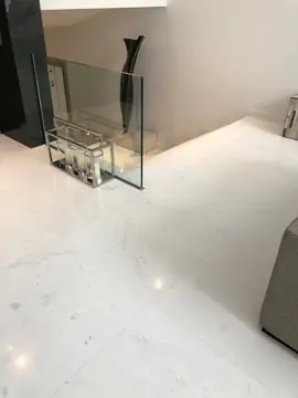 Suelo blanco junto al hueco de escalera. Pavimento blanco veteado en gran formato junto a la barandilla de vidrio y unos faroles decorativos.