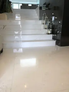 Escalera ancha con faroles. Escalera de peldaños blancos con veta gris sobre un pavimento pulido a juego, con faroles junto al paño oscuro.