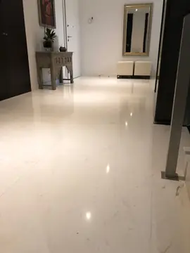 Recibidor con pavimento blanco pulido. Recibidor con suelo blanco pulido en piezas grandes, consola de madera tallada, pufs y espejo.