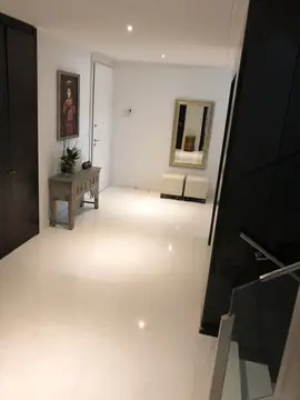 Recibidor visto desde la escalera. Recibidor con pavimento blanco pulido en gran formato entre armarios oscuros, con consola, cuadro y espejo.