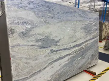 Tablero con veta azul y gris en exposición. Tablero pulido en tonos azul y gris claro con vetas onduladas, colocado en su caballete de exposición.
