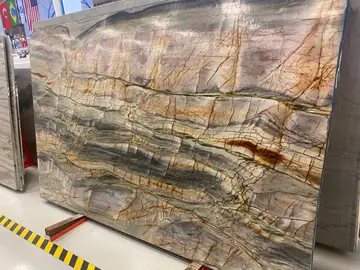 Tablero con vetas grises y rojizas. Tablero pulido de fondo claro cruzado por vetas grises, ocres y rojizas, en la nave de exposición.
