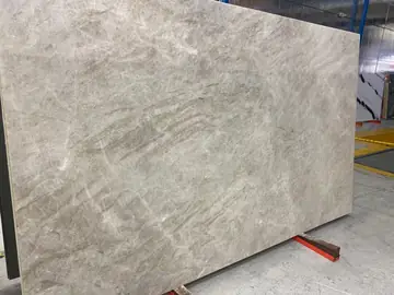 Tablero gris claro de veta suave. Tablero pulido en gris claro con vetas onduladas en tono beige, apoyado en caballete dentro de la nave.