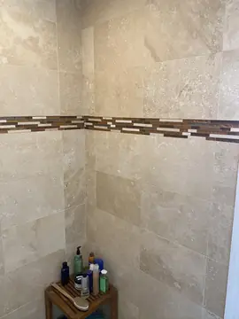 Rincón de ducha con cenefa de mosaico. Ducha revestida en piezas beige con una cenefa de mosaico en tonos marrón, crema y gris.