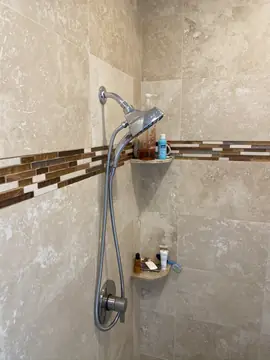 Pared de ducha con cenefa y repisas. Pared de ducha en piezas beige con cenefa de mosaico, repisas de rincón a juego y grifería con teleducha.