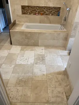 Baño con suelo en piezas de varios formatos. Pavimento en piezas beige de distintos tamaños combinadas, con bañera revestida y hornacina de mosaico al fondo.