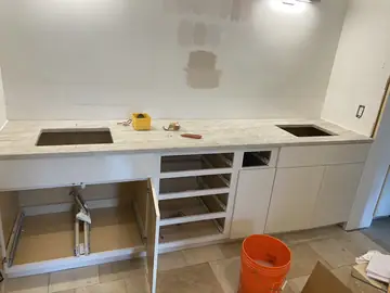 Encimera clara con dos huecos sobre el mueble. Encimera clara veteada con dos huecos rectangulares ya colocada sobre el mueble blanco, con los cajones todavía desmontados.