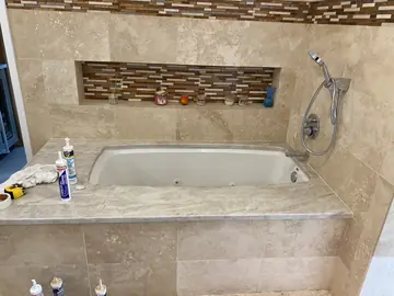 Bañera con la repisa nueva colocada. Repisa de bañera gris clara con veta suave recién colocada, con cartuchos de sellador y trapos todavía encima.