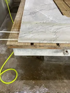 Pieza recién cortada en la mesa. Pieza blanca con veta gris recién cortada sobre la mesa de la cortadora, todavía mojada.