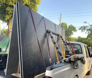 Tableros negros cargados en una camioneta. Tableros negros sujetos con cinchas a un caballete de madera en la caja de una camioneta, junto al carro de transporte.