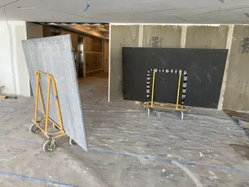 Tableros en carros listos para colocar. Un tablero gris veteado y otro negro de gran formato en carros, dentro de la sala con las paredes preparadas.