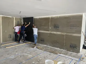 Colocación de pieza negra de gran formato. Operarios presentando una pieza negra de gran formato contra la pared forrada de placa de cemento.