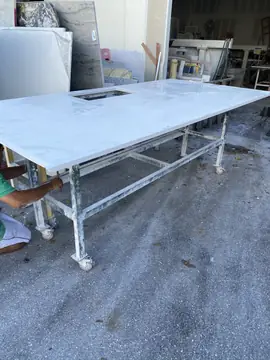 Encimera blanca con veta gris en su carro. Encimera blanca con veta gris y un hueco rectangular sobre carro metálico a la salida del taller.