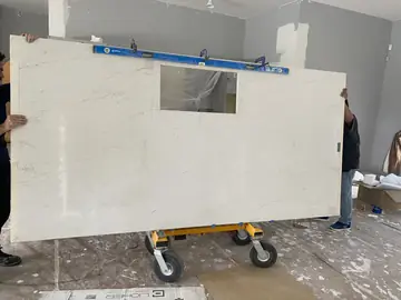 Traslado de encimera en carro. Encimera blanca con veta gris y hueco rectangular, en vertical sobre un carro, con un nivel sujeto con sargentos junto al borde superior.