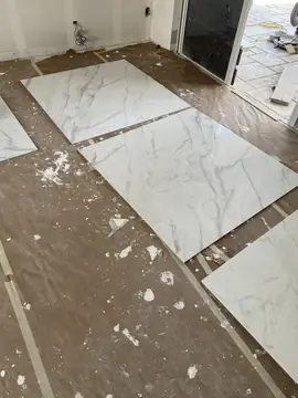Piezas blancas con veta gris sobre el suelo. Piezas blancas de gran formato con veta gris extendidas sobre el suelo protegido, junto a la puerta al exterior.