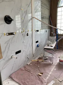 Revestimiento de baño durante la colocación. Pared de baño con piezas blancas de veta gris en gran formato, aún con niveladores y ventosa de colocación.